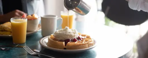 syrup pouring onto whipped cream on a waffle