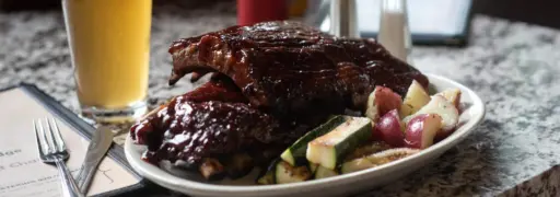 rack of BBQ ribs on a plate next to a beer